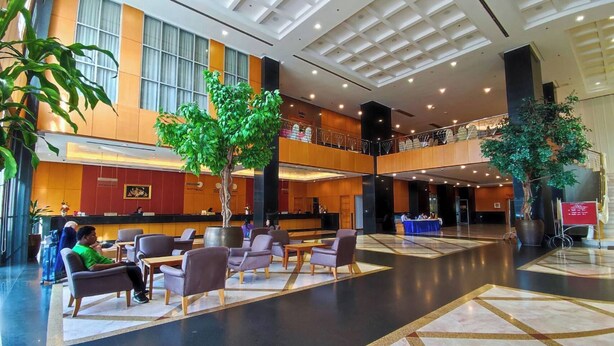 Een ruime lobby met verschillende zithoeken, een receptiebalie en grote kamerplanten.