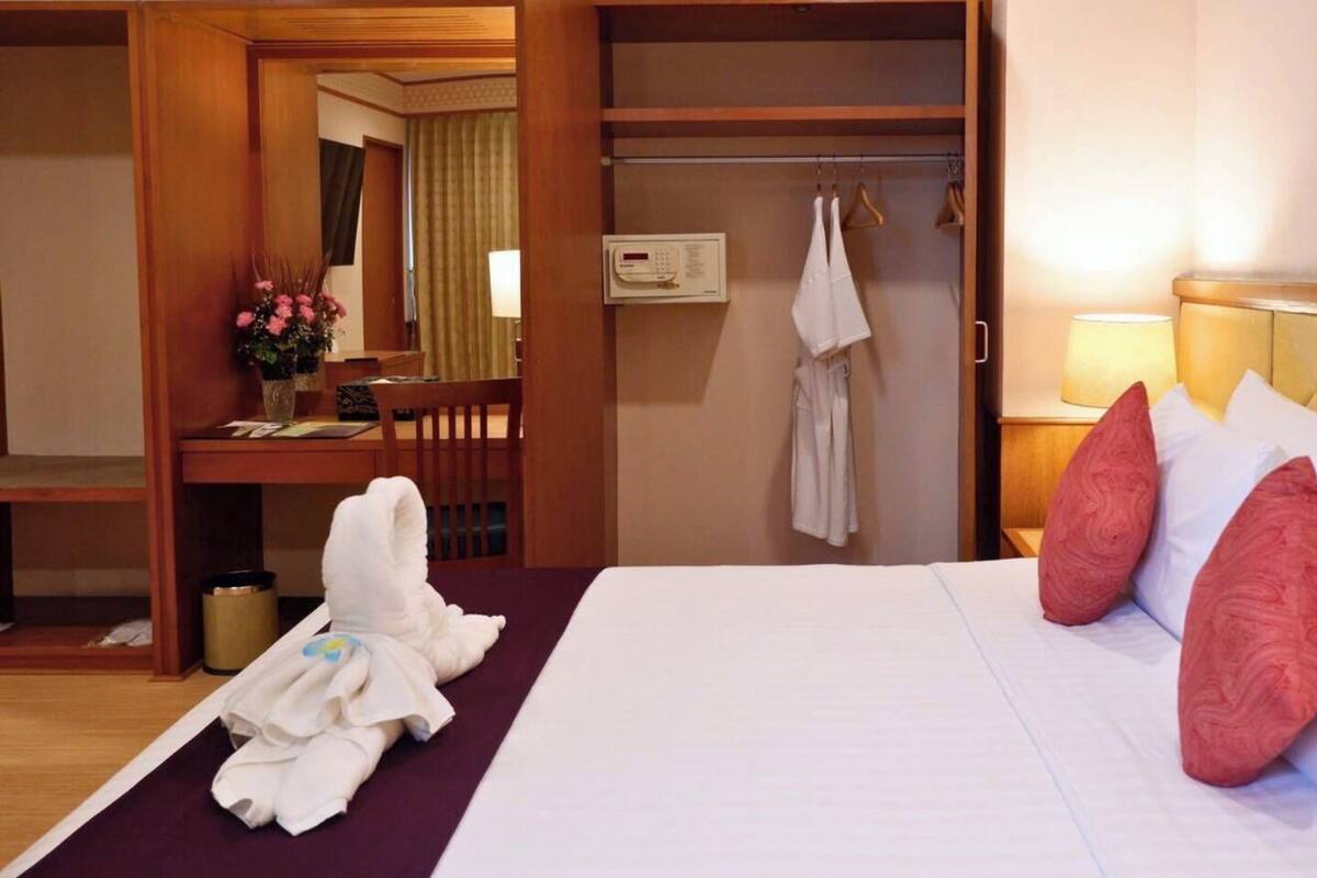 Een hotelkamer met een groot bed, een houten garderobe, een bureau met stoel en een spiegel.