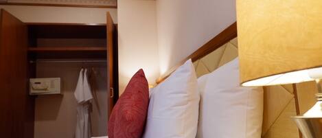 Une chambre d’hôtel avec un lit, un oreiller rouge et blanc, une lampe et une armoire contenant une robe et un panneau de commande.