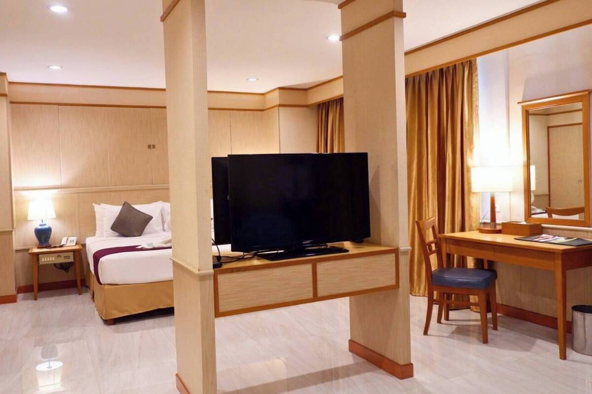 Een hotelkamer met een bed, een bureau met stoel, een televisie, een lamp en een spiegel.