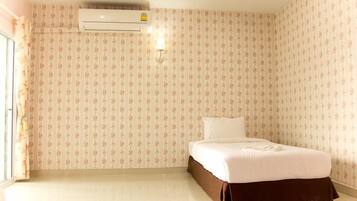 Habitación de hotel con papel tapiz floral, cama con cubrecama blanco y unidad de aire acondicionado en la pared.