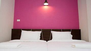 A double bed with white linens, a dark headboard, and a pink wall.