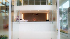 Un área de recepción moderna con un panel de vidrio, una mesa de recepción y un arreglo floral decorativo.