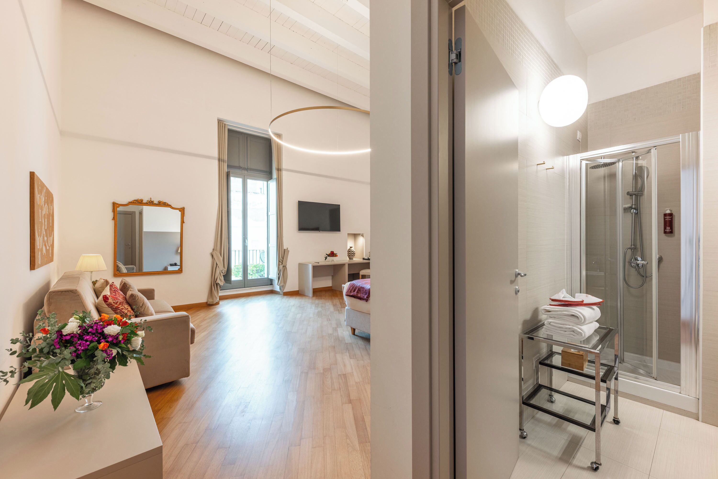 Habitación de hotel moderna con zona de estar, cabina de ducha de vidrio y una mesita con toallas.