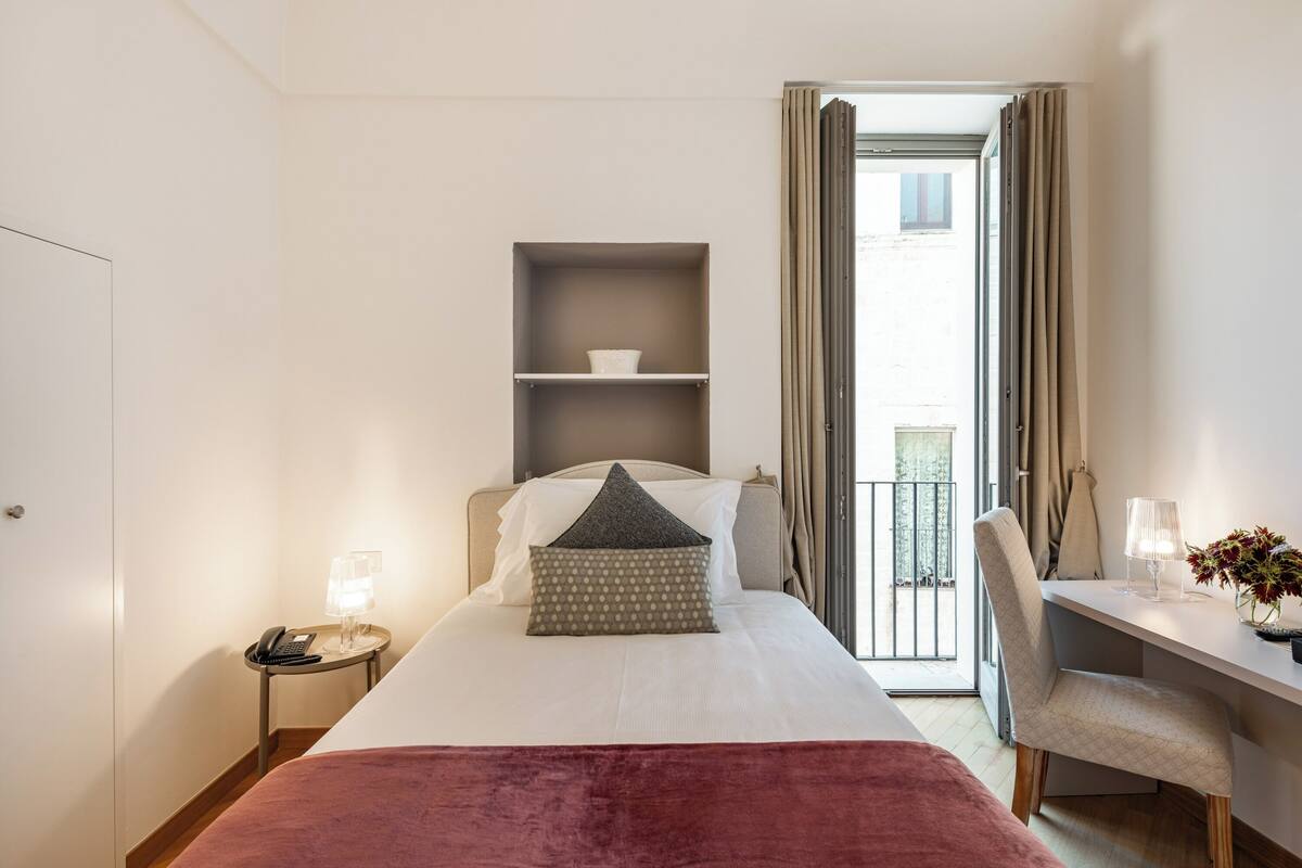 Una habitación de hotel con cama, mesita de noche, lámpara y escritorio con silla.