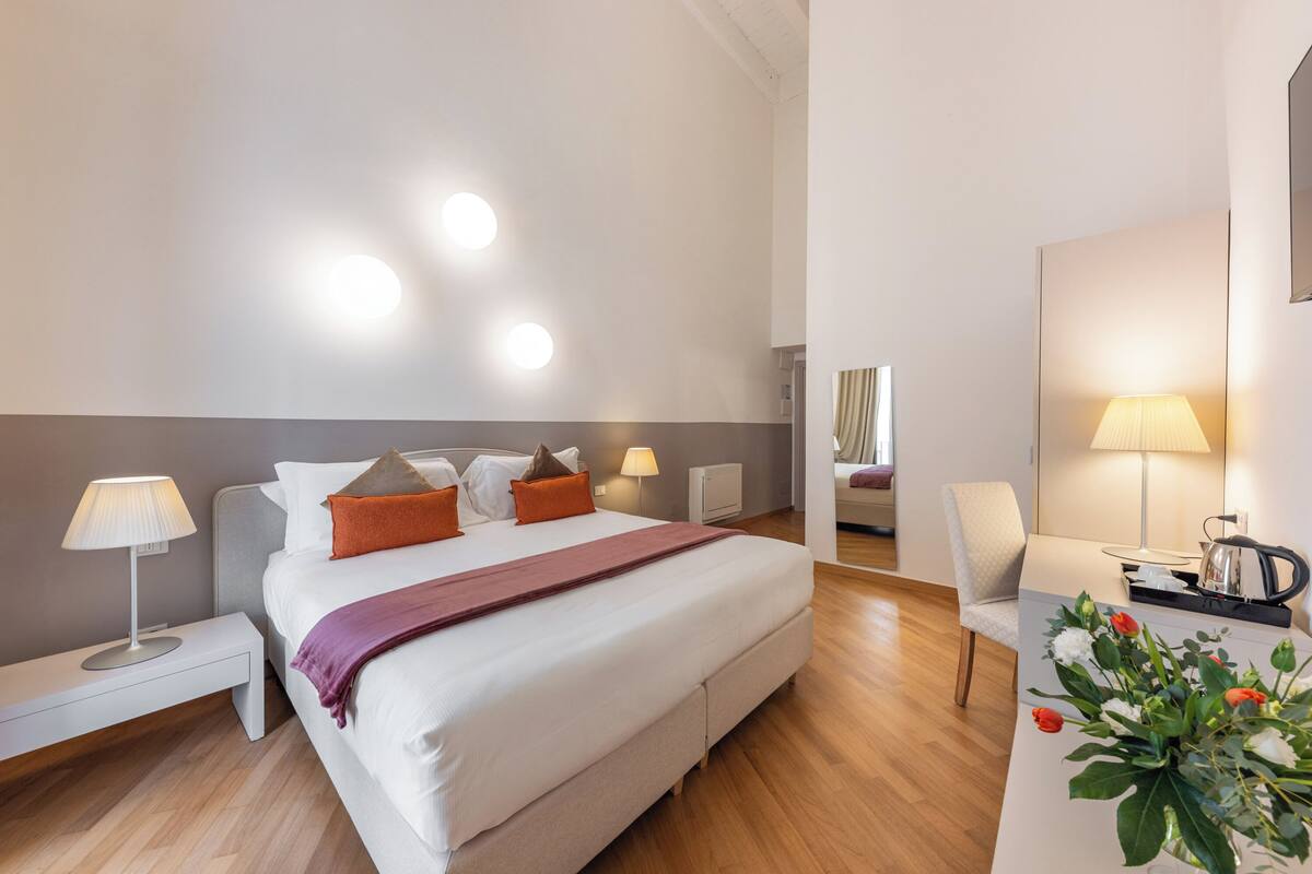 Una habitación de hotel moderna con una cama grande, mesitas de noche con lámparas, un escritorio con lámpara y una silla.
