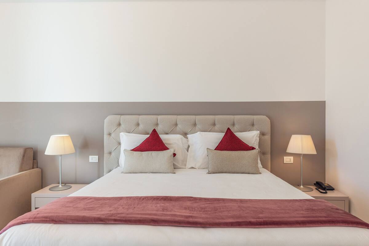 Una habitación de hotel ordenada con una cama grande, dos mesitas de noche y una manta roja.