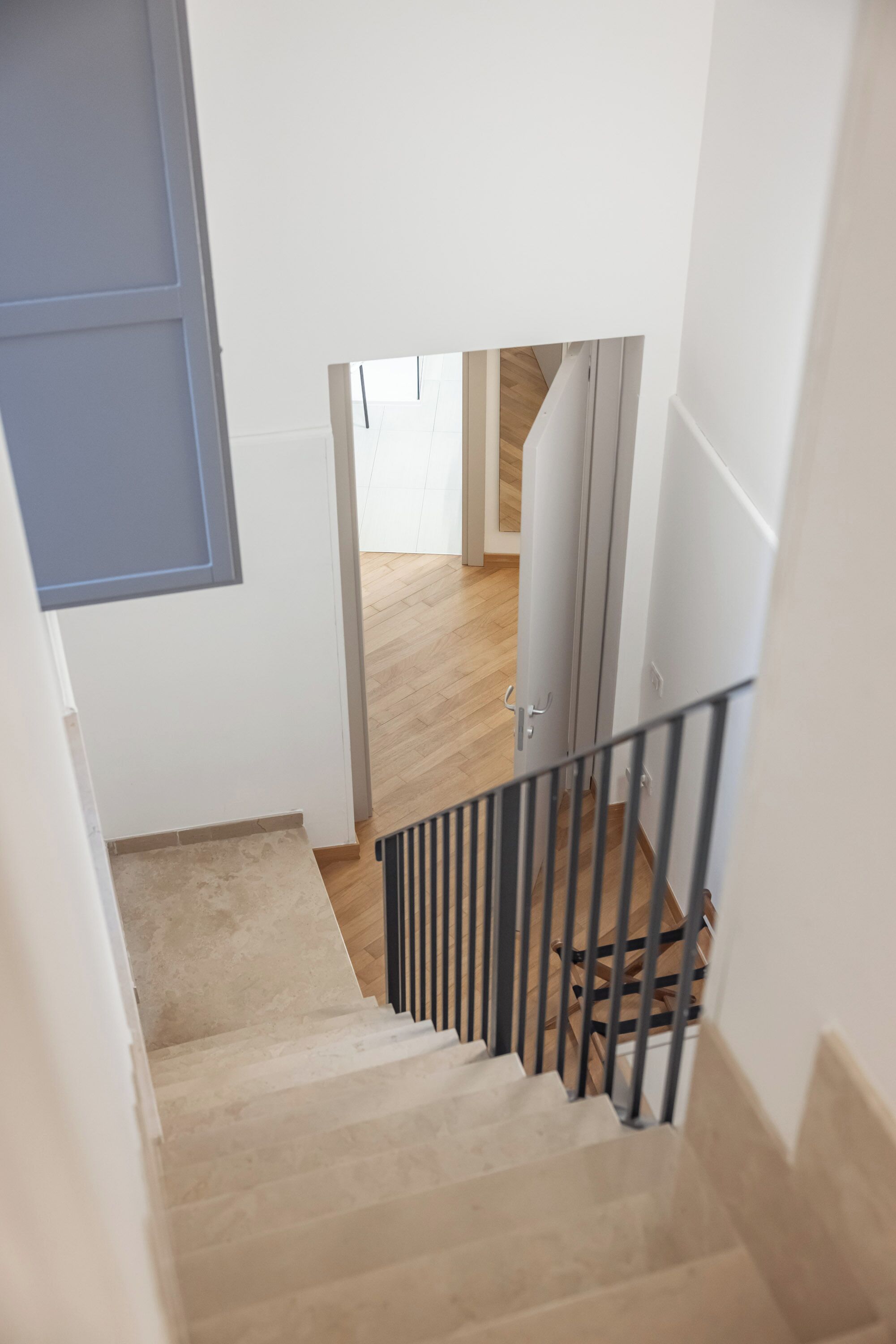 A staircase with beige steps and a metal railing, leading to a room with wooden flooring and a white door.