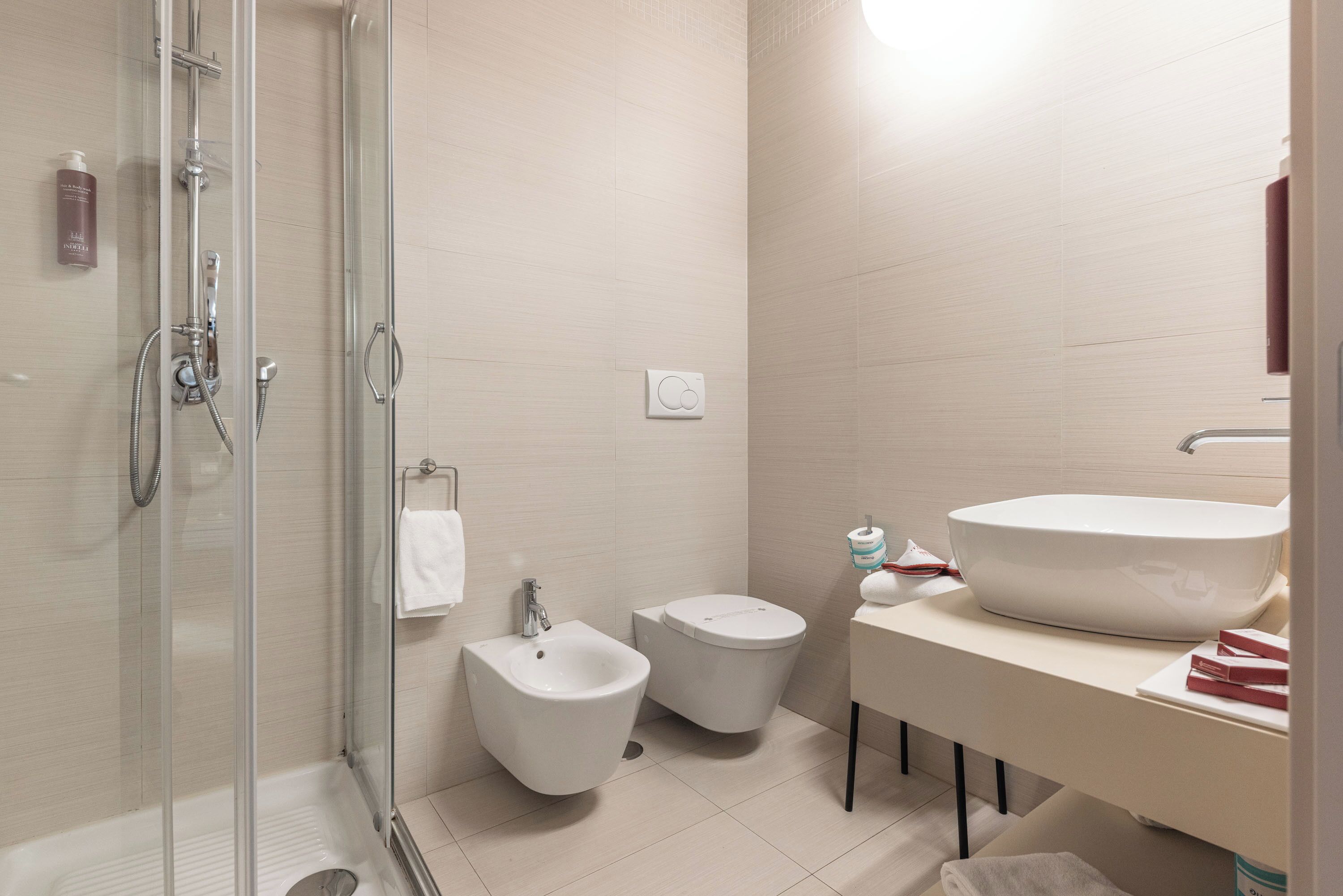 Un baño moderno con cabina de ducha de vidrio, un bidé, un inodoro y un lavamanos grande con espejo.
