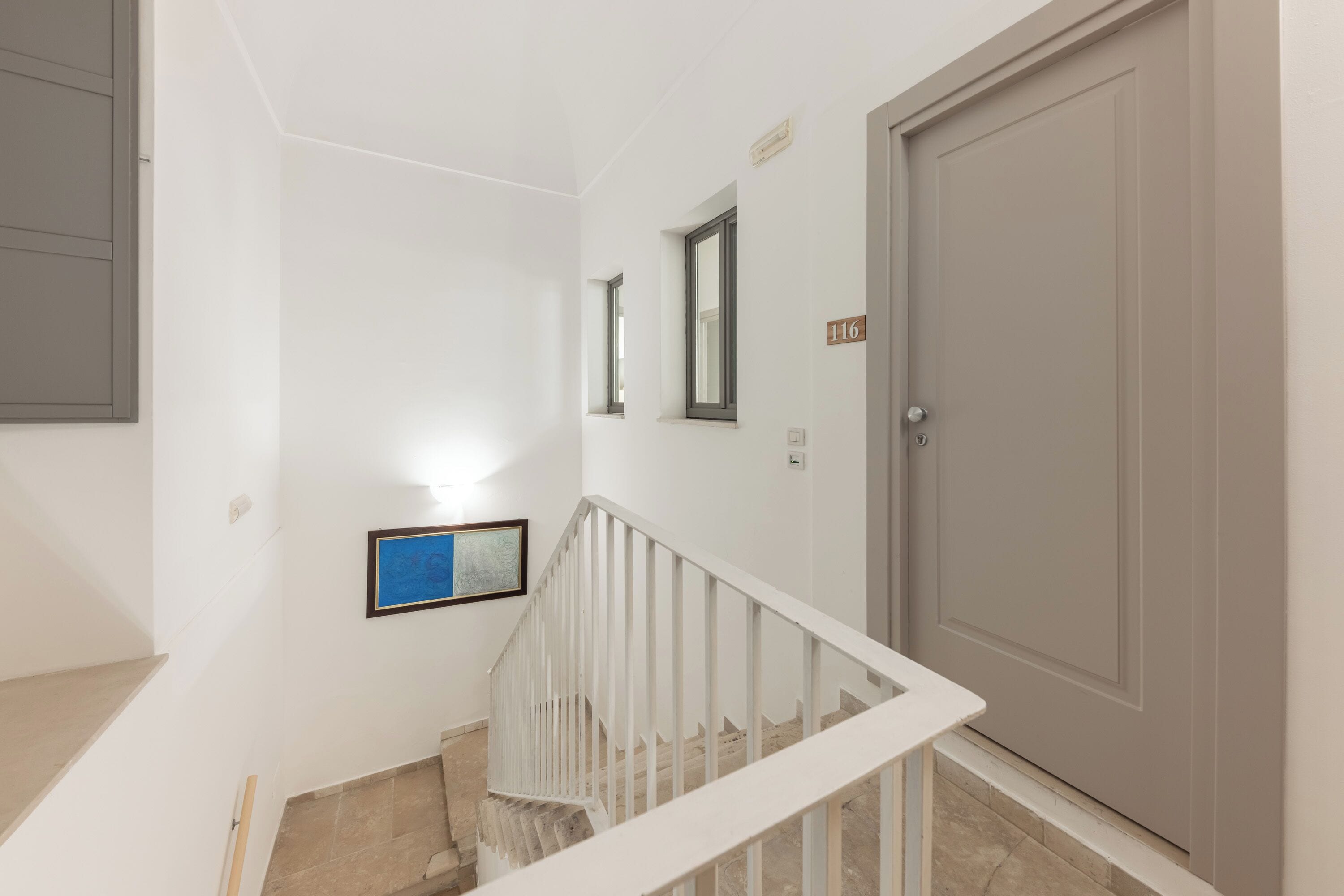 Un escalier avec des rampes blanches menant à une porte portant le numéro 116.