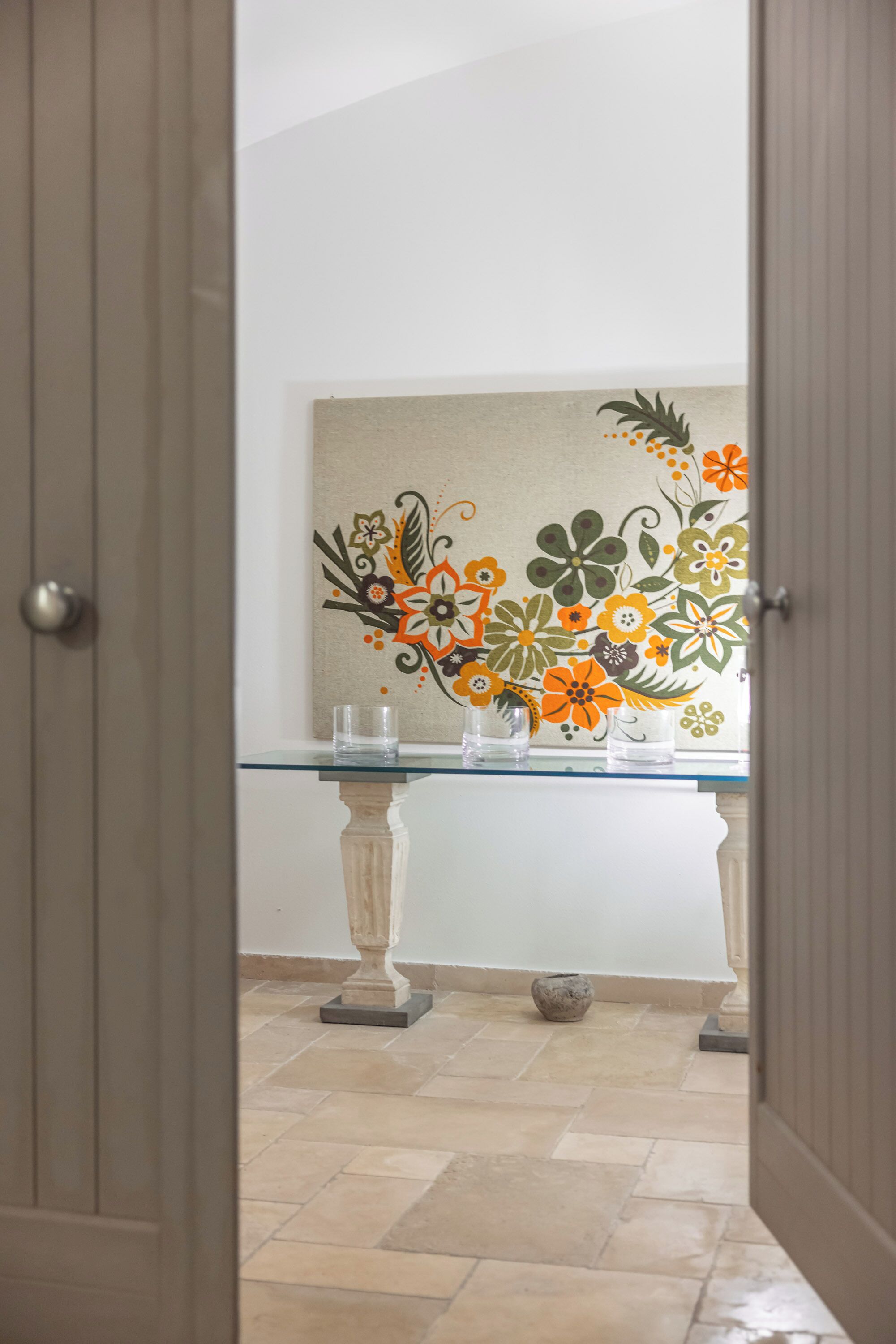 A hallway with a glass-top table, a decorative floral wall, and a tiled floor.