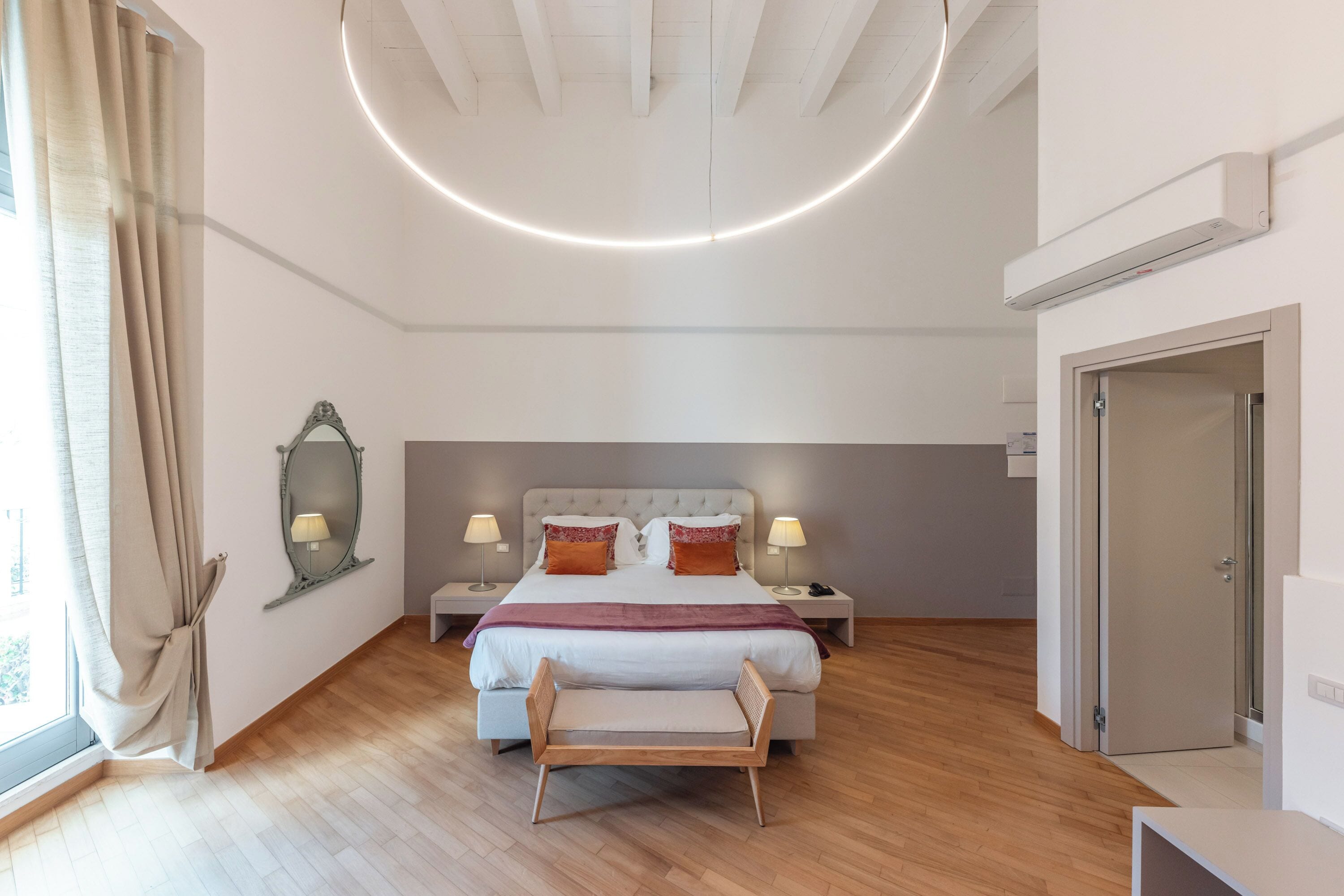 A modern bedroom with a large bed, bedside lamps, a mirror, and a bench.