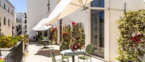 Un área de patio con mobiliario exterior, sombrillas blancas y plantas en macetas.