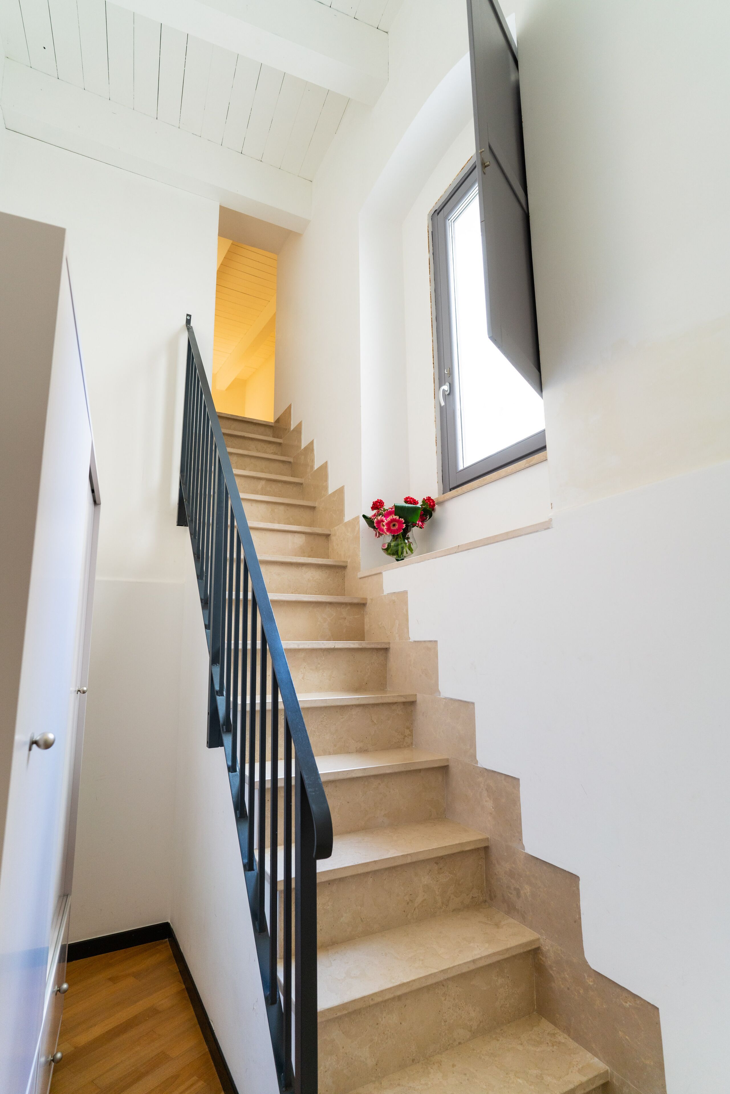 A staircase with beige steps and a black railing, leading to a room with a window and a door.
