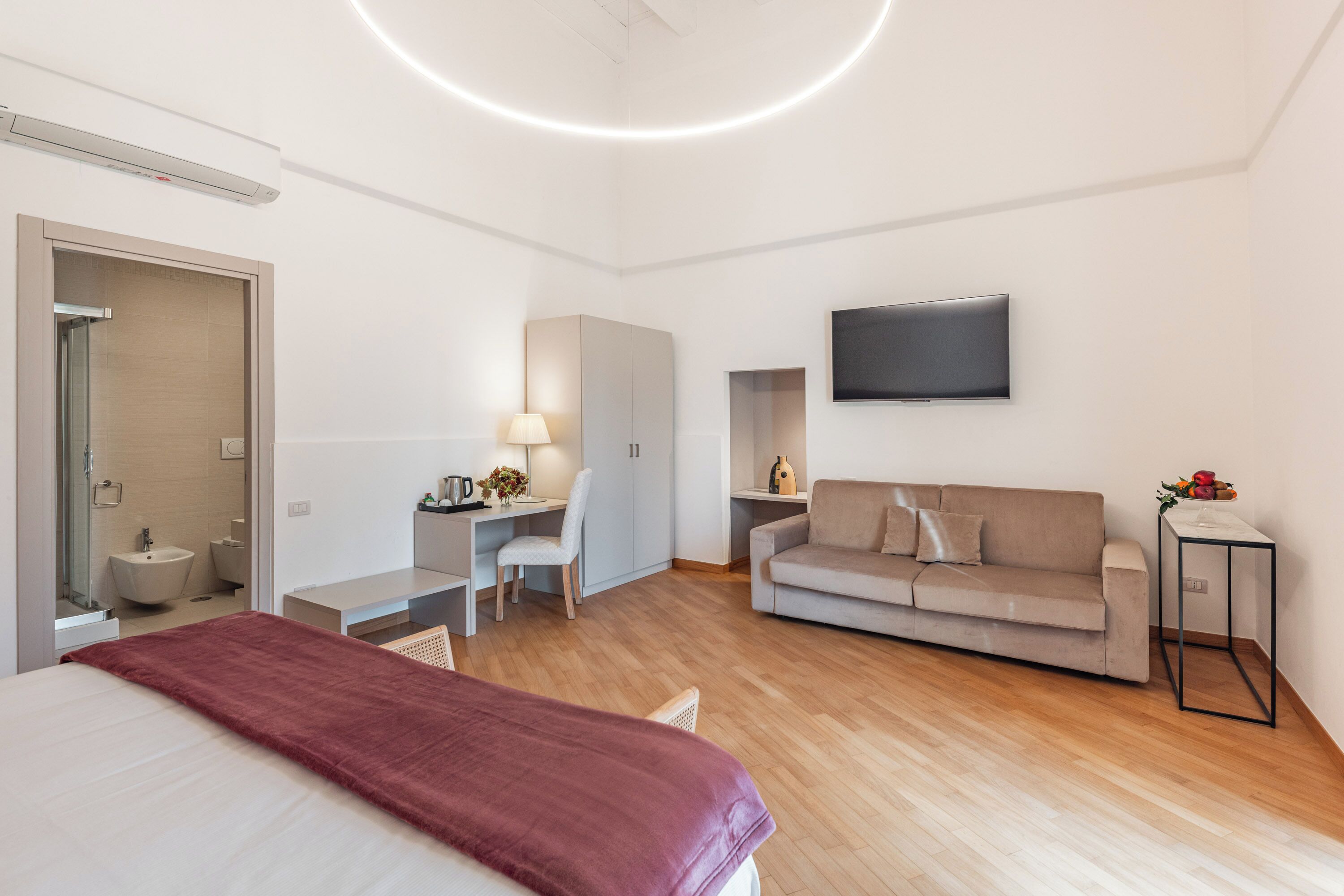 Moderni hotellihuone, jossa on sänky, työpöytä, sohva, televisio ja kylpyhuone.