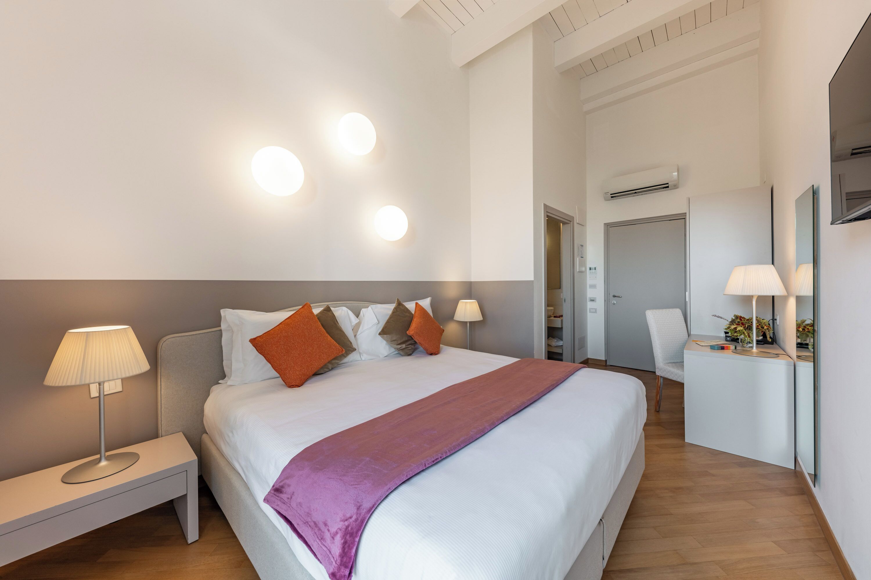 Una habitación de hotel moderna con una cama grande, lámparas de noche, un escritorio y una silla.