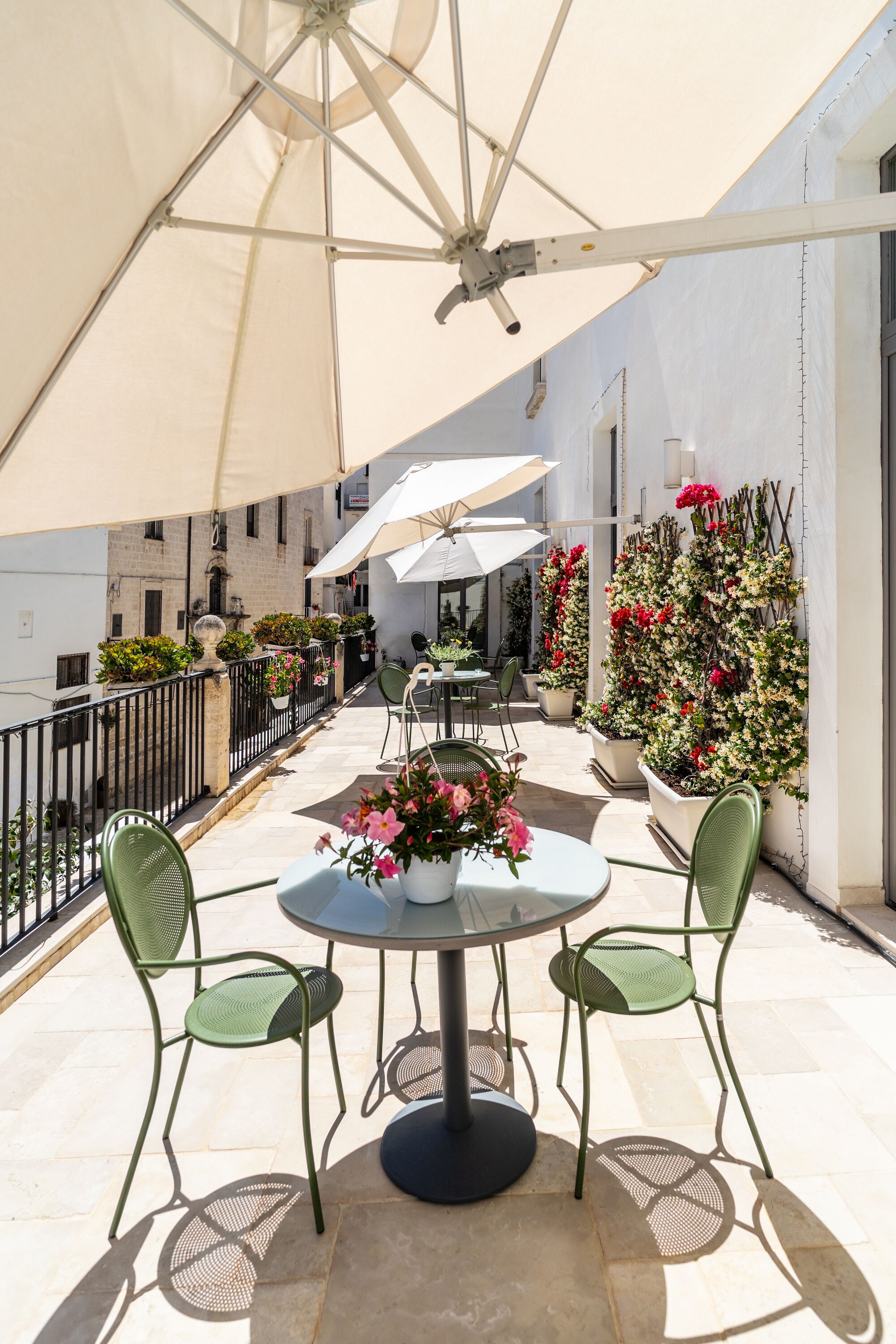 An outdoor patio with a round table and two chairs, surrounded by potted plants and a large umbrella.