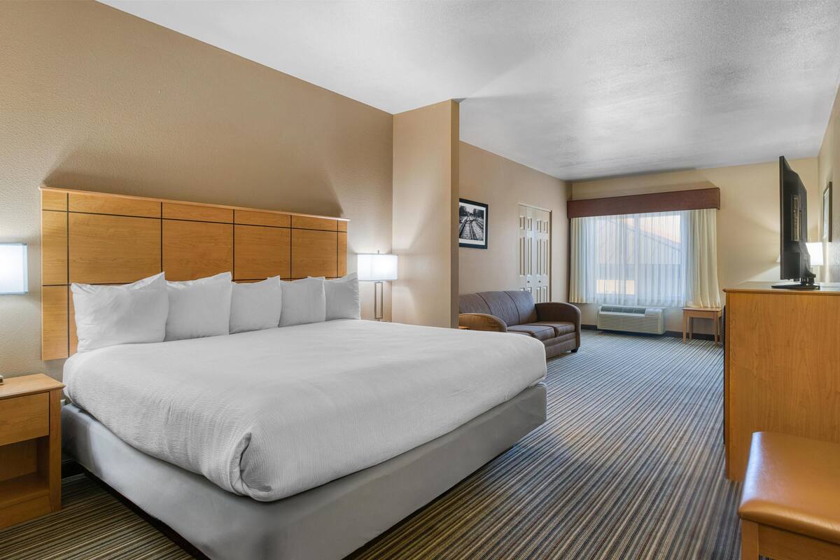 Ein Hotelzimmer mit einem großen Bett, einem Holzkopfschild, einem Schreibtisch, einem Stuhl und einem Fernseher.