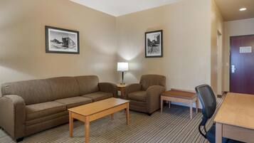 A hotel room with a sofa, armchair, small table, lamp, and a desk with a chair.