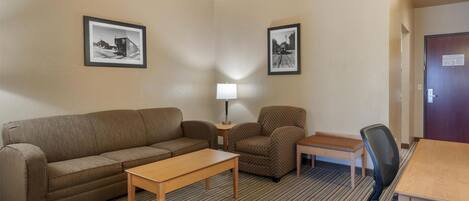 Habitación de hotel con sofá, sillón, mesita, lámpara y escritorio con silla.