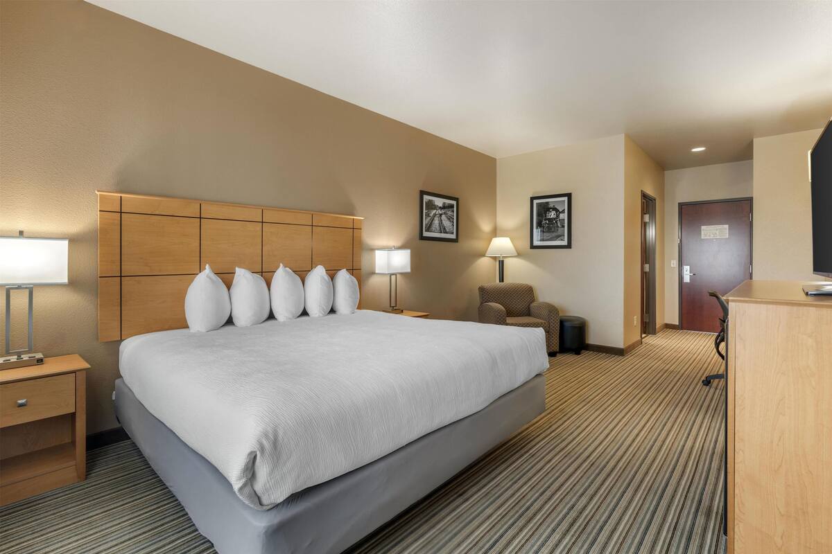 Ein Hotelzimmer mit einem großen Bett, zwei Nachttischen mit Lampen, einem Sessel und einem Schreibtisch.