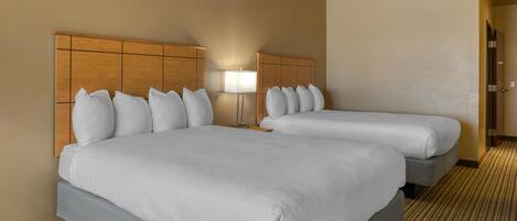 A hotel room with two beds, a wooden headboard, a lamp, and a carpeted floor.
