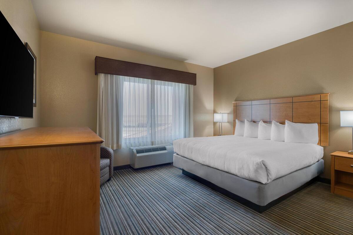 Ein Hotelzimmer mit einem großen Bett, einem Fernseher, einem Schreibtisch und einem Fenster mit Vorhängen.