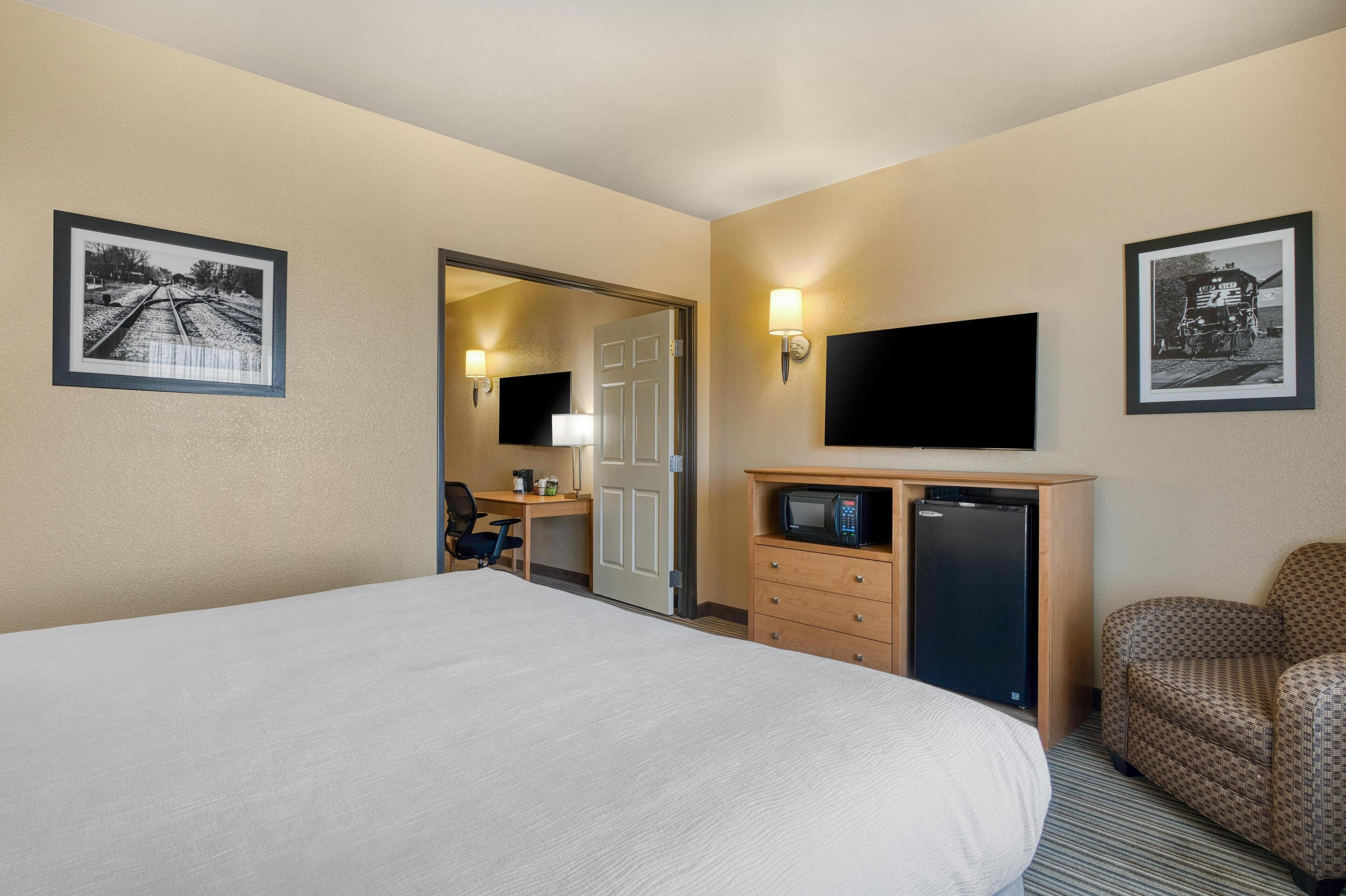 A hotel room with a large bed, a desk with a chair, a microwave, a television, and two framed pictures on the walls.