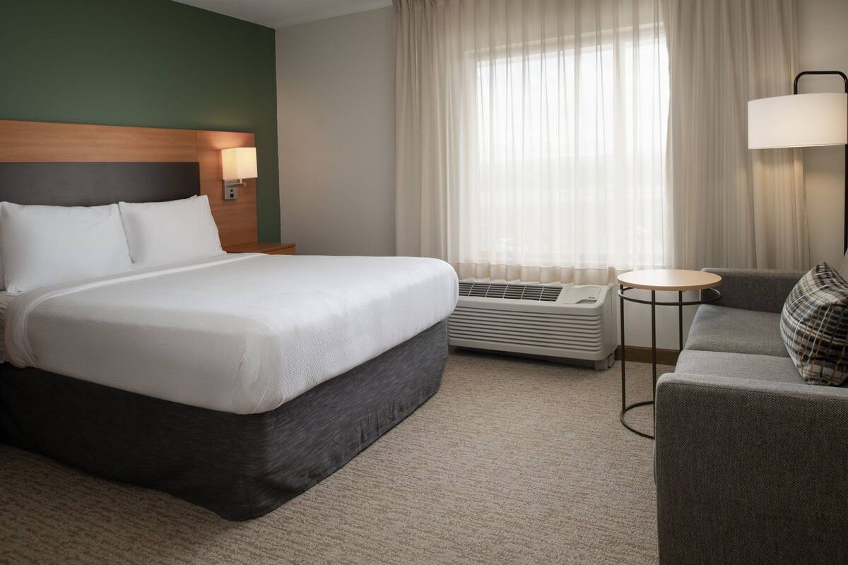 Een hotelkamer met een groot bed, een kleine zithoek, een tafel en een raam met gordijnen.