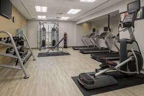 Une salle de sport équipée de tapis de course, de vélos elliptiques, d’haltères et d’appareils de musculation.