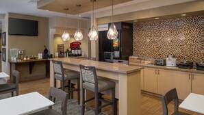 Una cocina moderna con barra desayunadora, taburetes y una zona para preparar café.