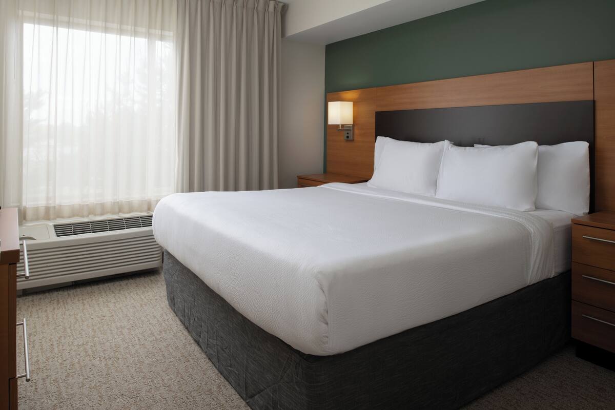 Een hotelkamer met een groot bed, een nachtkastje, een lamp en een raam met gordijnen.