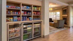 Un vestíbulo de hotel con estantes llenos de aperitivos de diferentes marcas y un expositor refrigerado con bebidas.