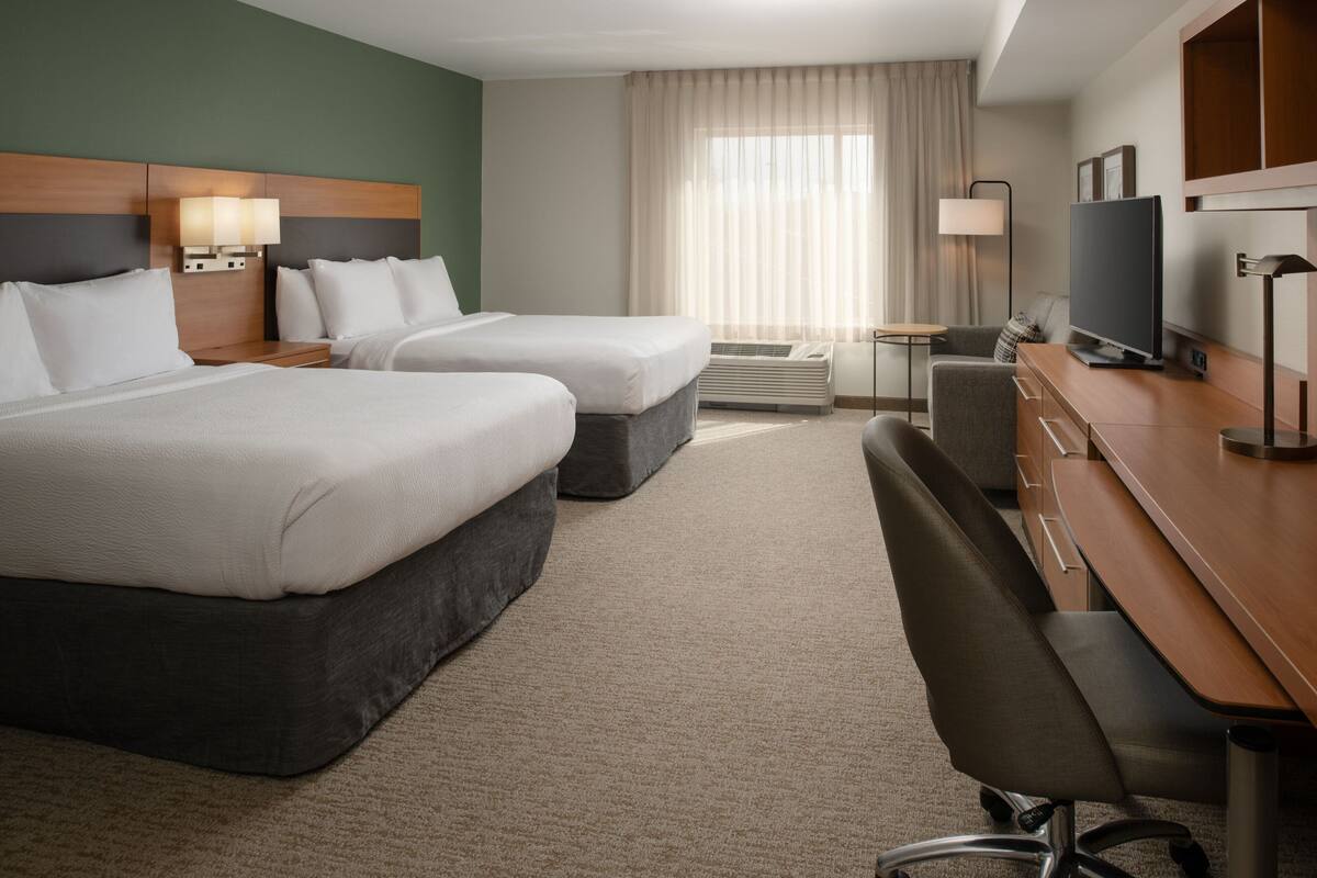Hotelkamer met twee bedden, een bureau, een stoel, een televisie en een raam met gordijnen.