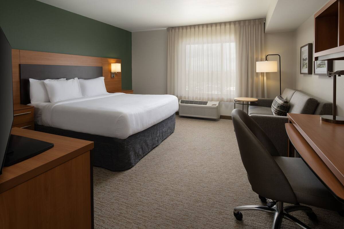 Hotelkamer met een groot bed, een bureau, een stoel, een airconditioner en een raam met gordijnen.