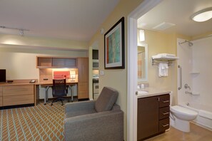 Une chambre d’hôtel compacte comprenant un coin cuisine, un canapé, une salle de bain avec douche et un petit espace bureau.