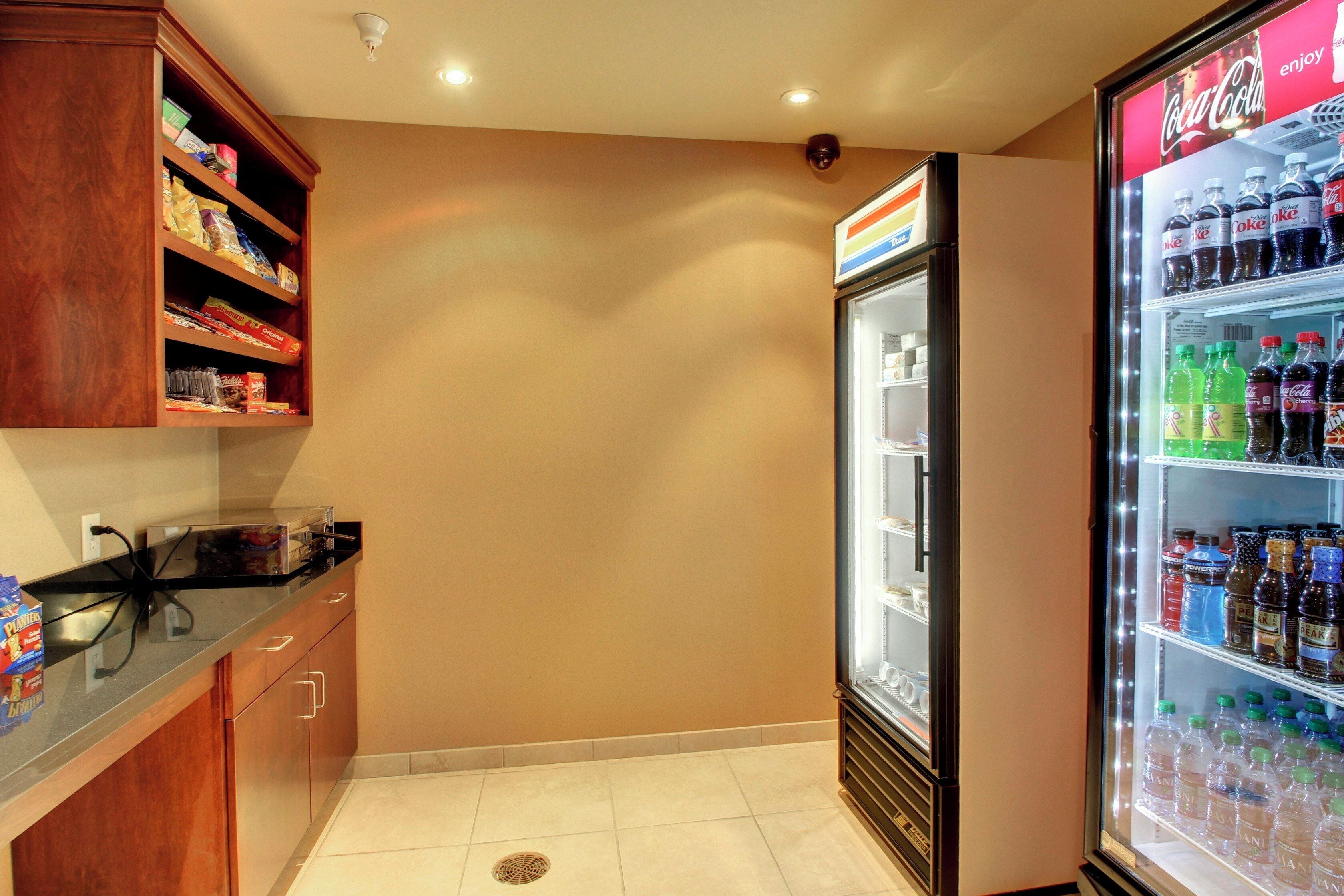 Una kitchenette equipada con un refrigerador lleno de bebidas, un microondas y una alacena con aperitivos.