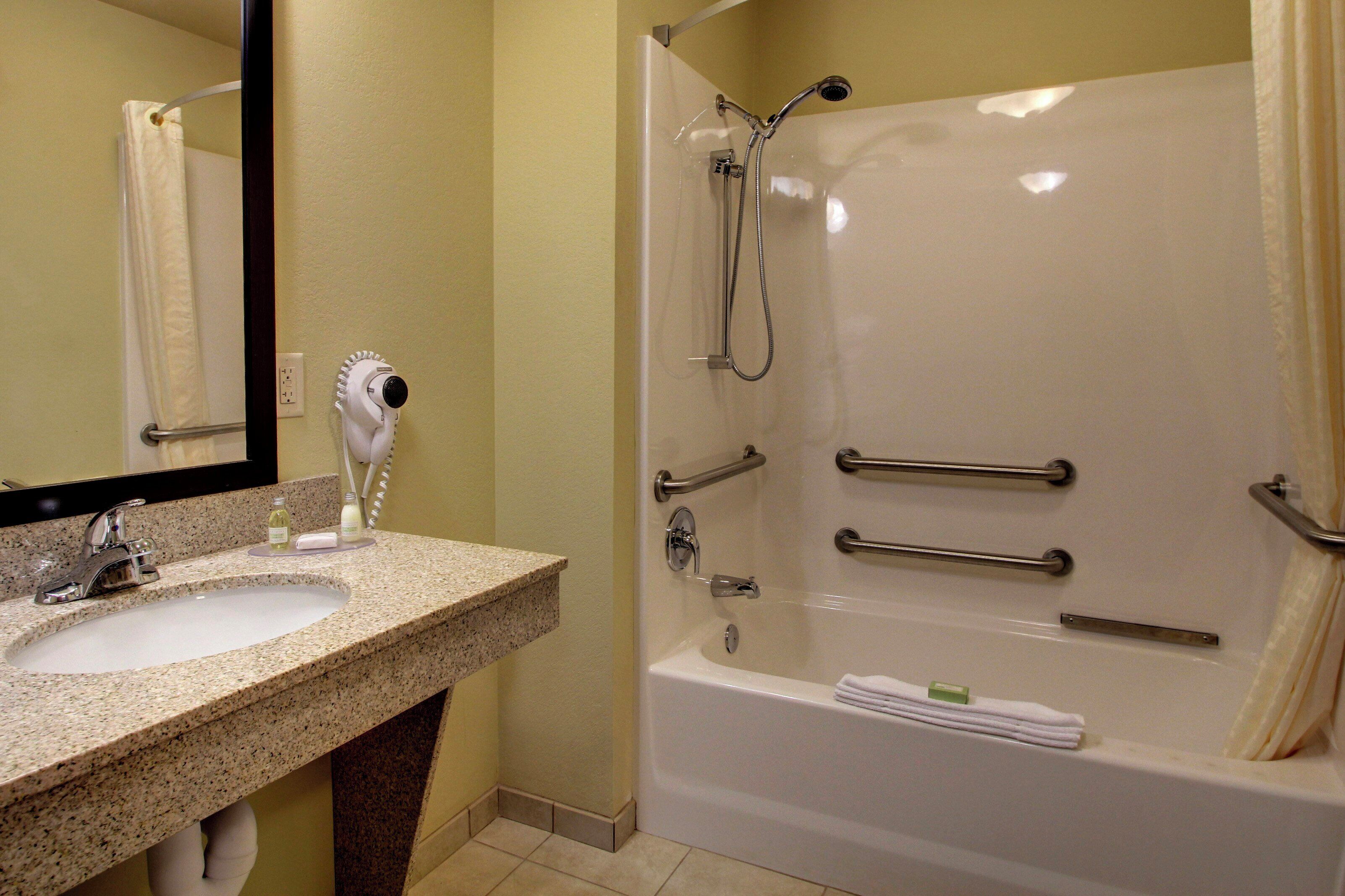A bathroom with a sink, mirror, and a walk-in shower with grab bars.