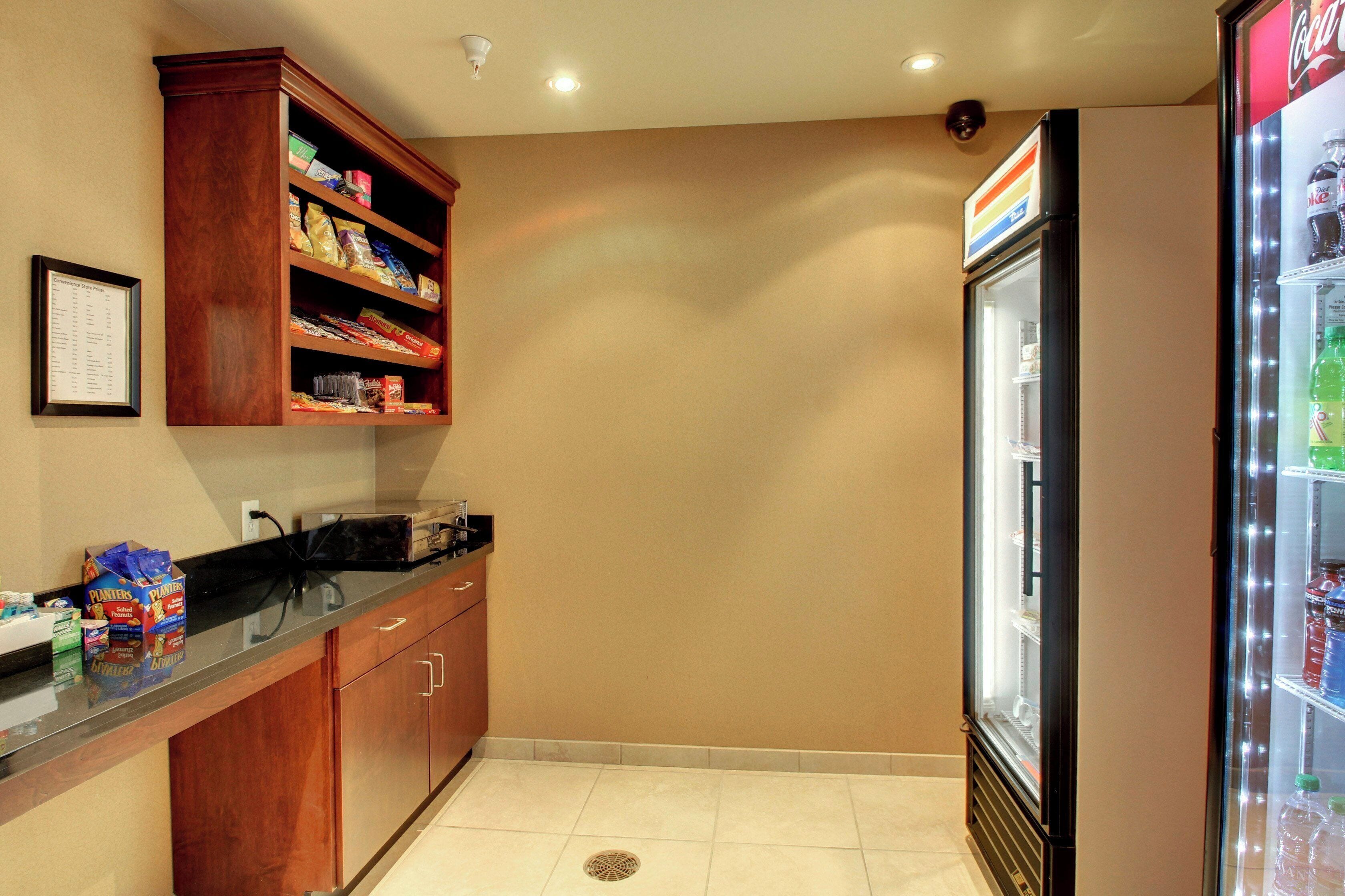 A kitchenette with a refrigerator, a microwave, and a shelf stocked with snacks.