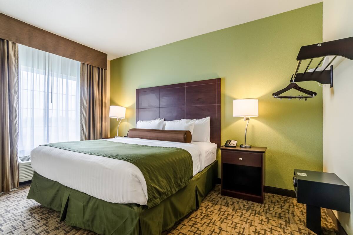 Une chambre d’hôtel avec un grand lit, deux lampes de chevet, une table de chevet et un porte-manteau.