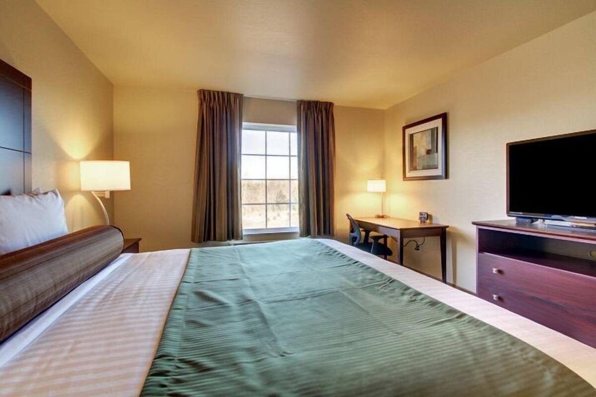Une chambre d’hôtel équipée d’un lit, d’un bureau, d’une chaise, d’une télévision et d’une fenêtre avec des rideaux.
