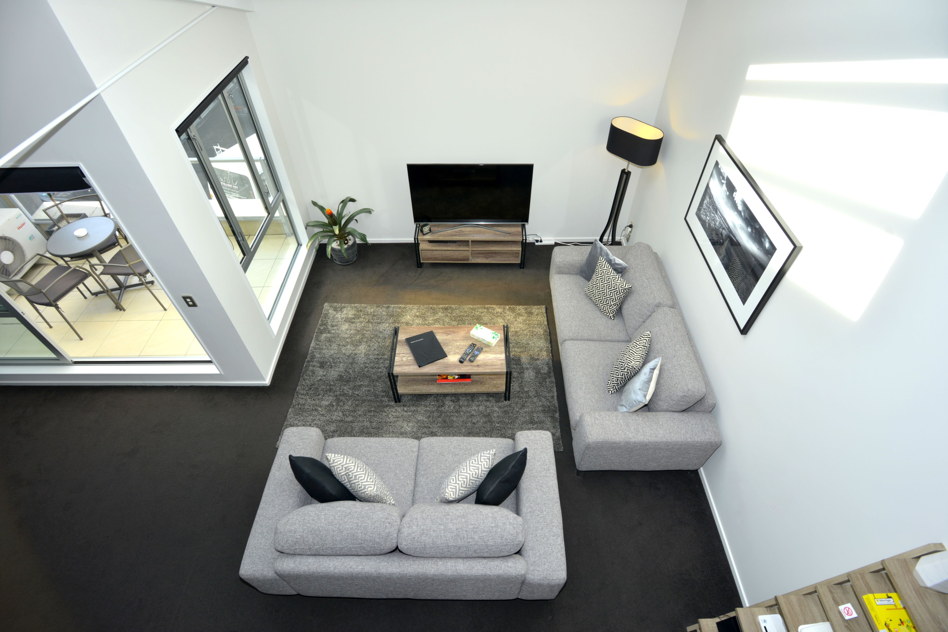 A modern living room with a grey sofa, a coffee table, and a TV. There is a dining area with a table and chairs visible through an open door.