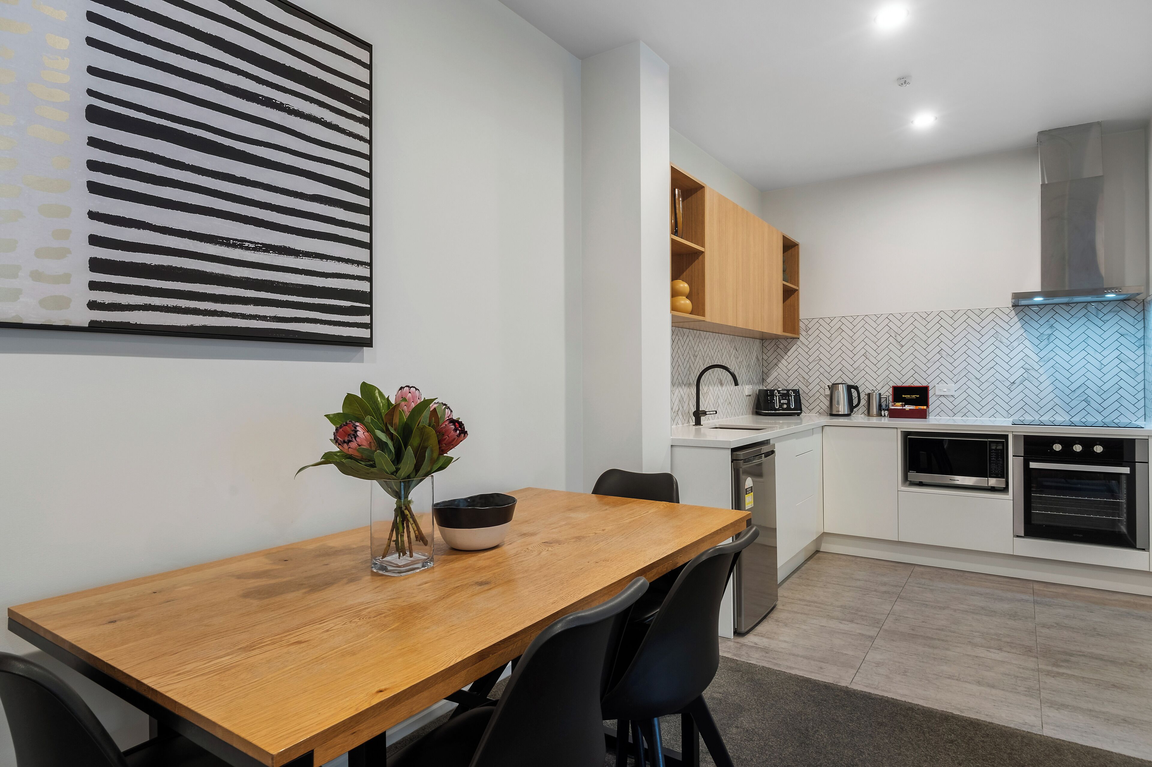A modern kitchen with white cabinets, a wooden dining table, and a black and white striped wall art piece.