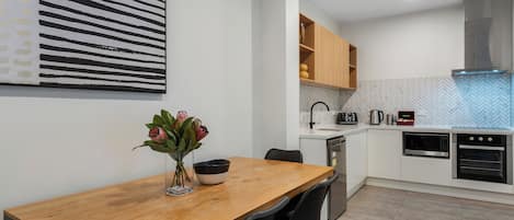 A modern kitchen with white cabinets, a wooden dining table, and a black and white striped wall art piece.