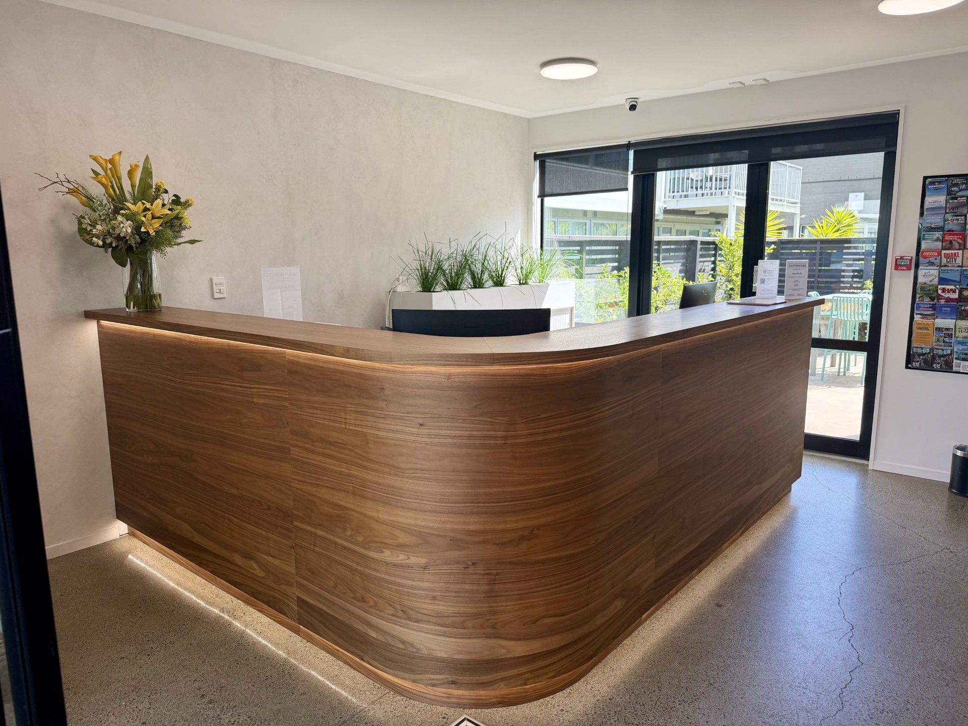 Un comptoir d’accueil avec un revêtement en bois, une plante en pot et une fenêtre donnant sur l’extérieur.