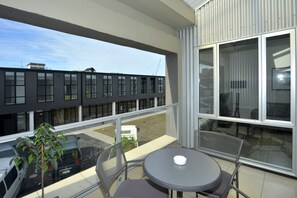 Een balkon met een tafel en stoelen, een uitzicht op een modern gebouw en geparkeerde auto's.