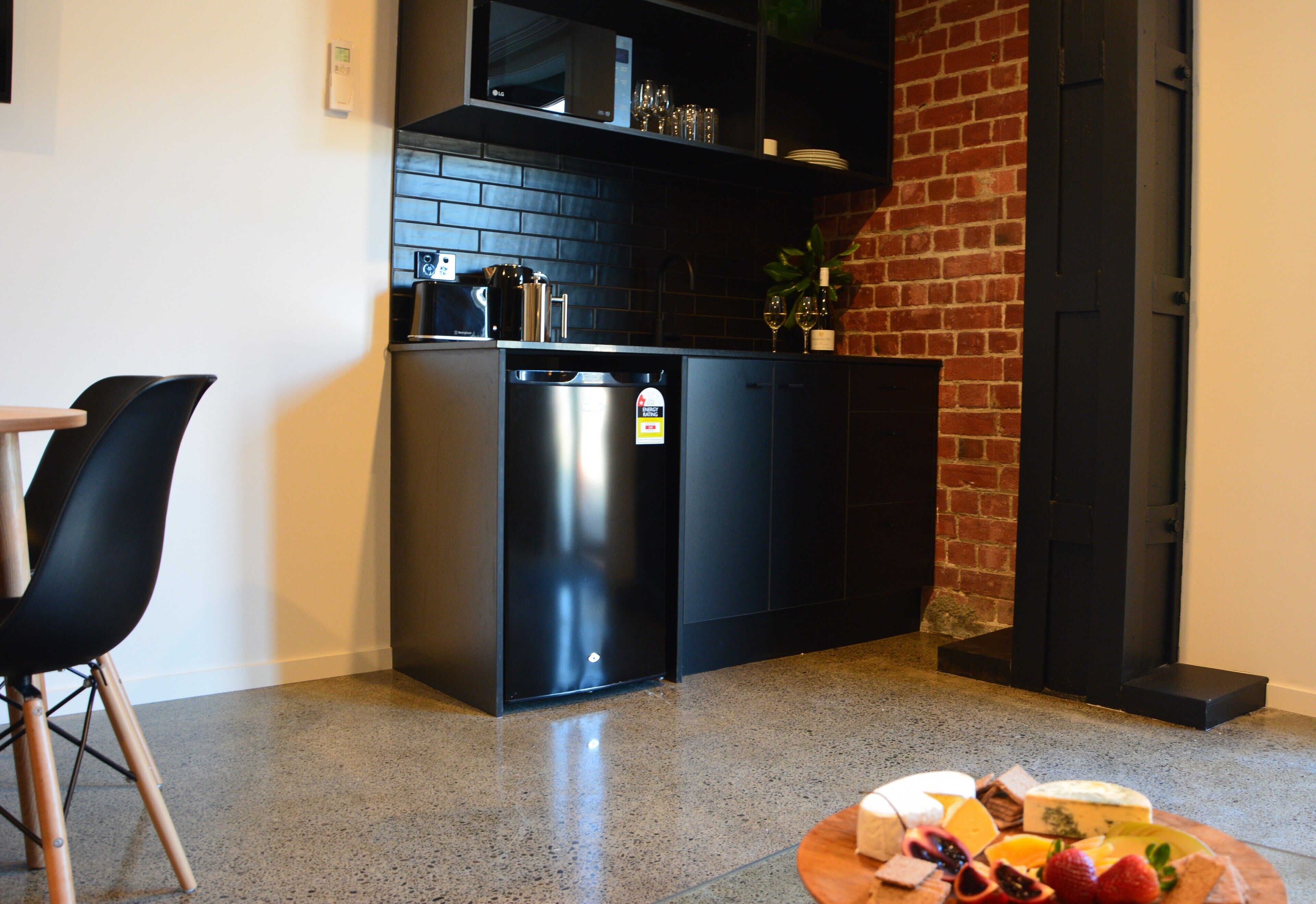 A compact kitchen with a black refrigerator, a microwave, and a brick wall.