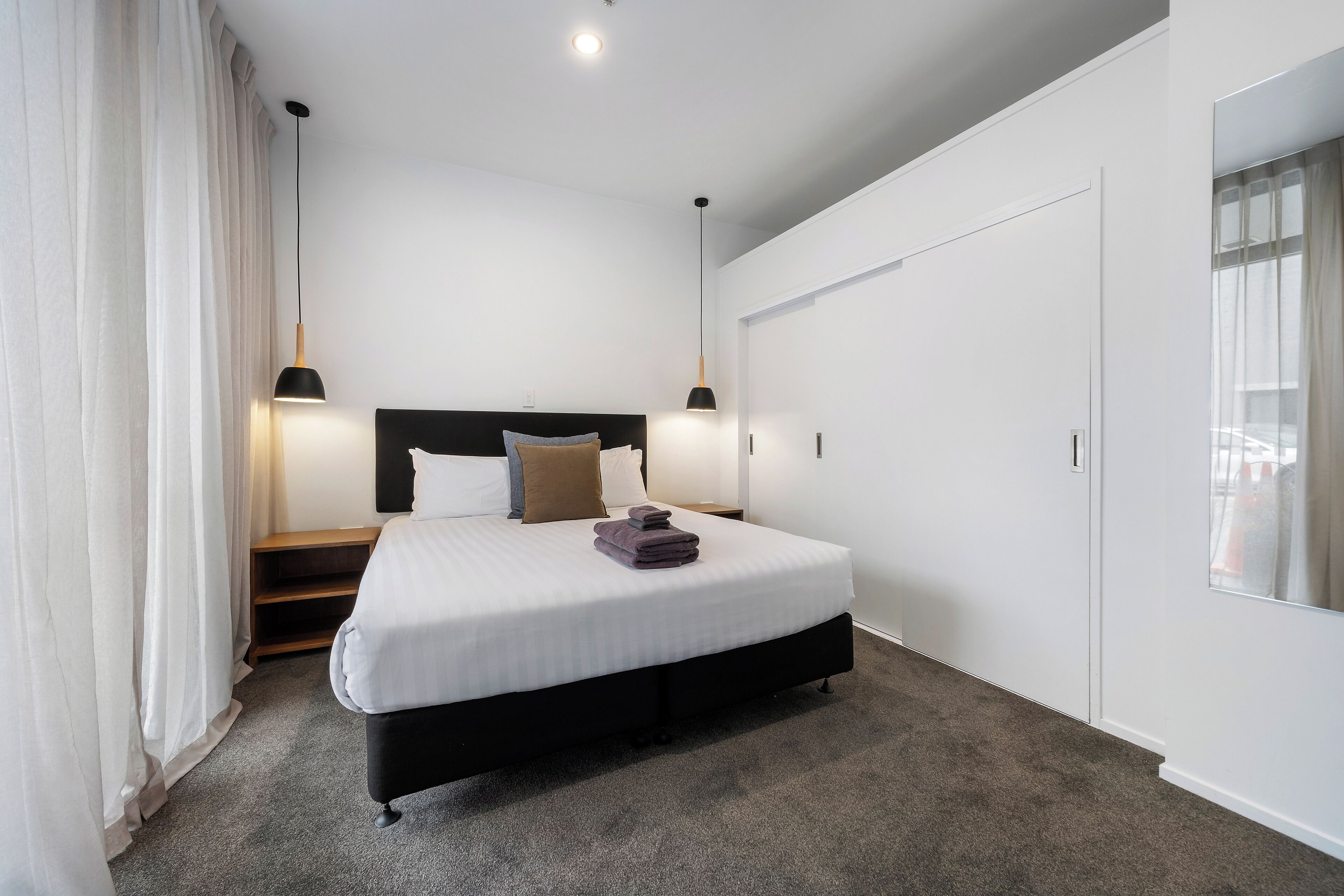 A modern hotel room with a large bed, a nightstand, a wardrobe, and a window with curtains.