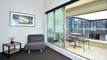 A modern room with a grey sofa, a small table with a plant, and a large sliding glass door leading to an outdoor patio with a table and chairs.