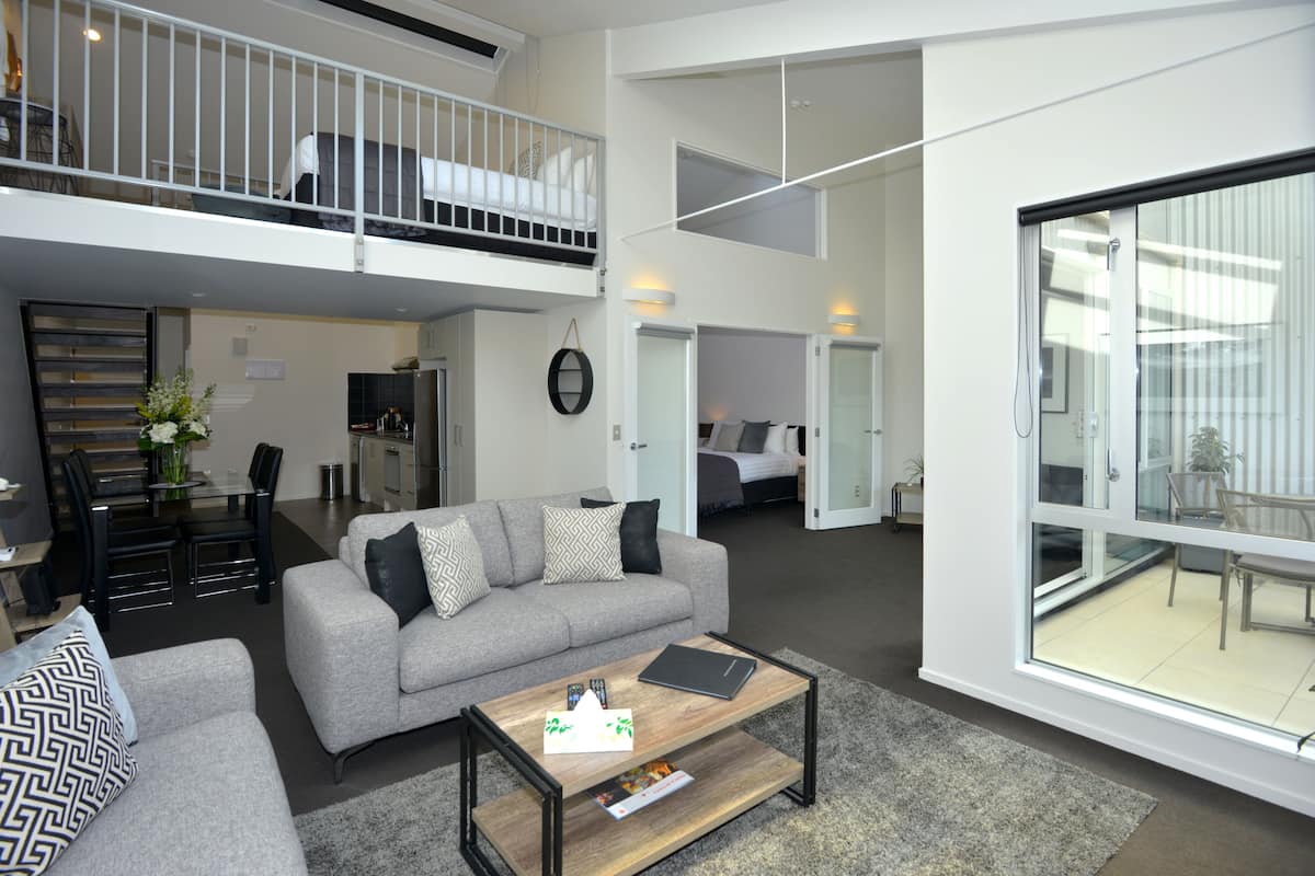 Un appartement moderne avec un canapé gris, une table basse et un balcon doté d’une rambarde.